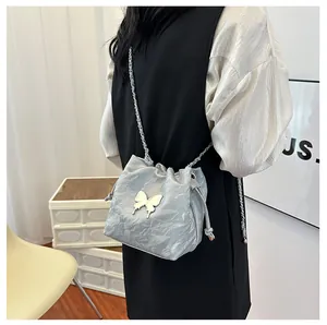 Détail du sac seau argenté avec papillon et bandoulière chaîne porté par un mannequin