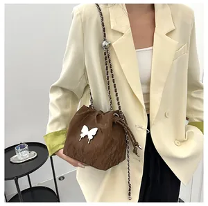 Détail du sac seau marron foncé avec boucle papillon et bandoulière sur un mannequin