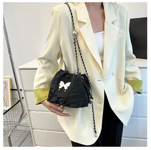 Détail du sac seau plissé noir avec papillon et bandoulière en chaîne tressée