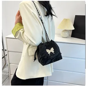 Sac seau noir à cordon avec chaîne papillon argentée sur un blazer beige chic