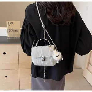 Vue détaillée du sac à bandoulière matelassé gris clair avec pendentif en peluche et chaîne
