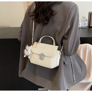 Petit sac blanc texturé avec bijou en peluche porté sur un blazer gris foncé chic