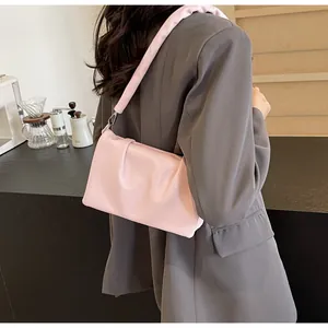 Détail du sac bandoulière plissé rose clair porté par un mannequin en blazer gris