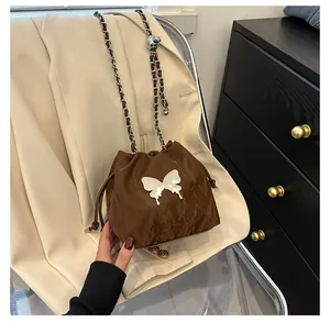 Détail du sac seau marron foncé avec cordon, papillon argenté et bandoulière chaîne