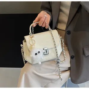Détail d'un sac crème avec chaîne argentée, cuir matelassé et pompon en peluche