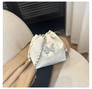 Détail du sac seau crème avec breloque papillon et bandoulière en chaîne argentée