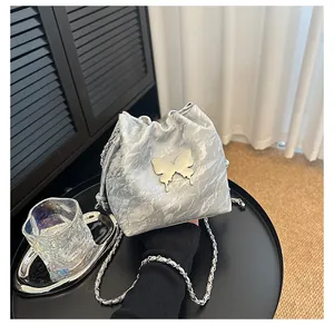 Détail du sac seau argenté à cordon avec grand papillon métallique et bandoulière chaîne
