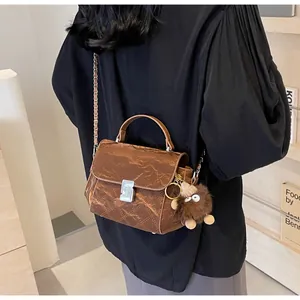 Détail d'un sac bandoulière matelassé marron avec chaîne en métal et breloque peluche