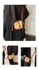 Détail du sac seau en paille tressée avec bordures en cuir marron et boucles dorées