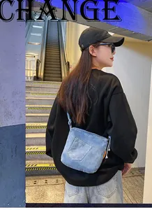 Detail of light blue denim crossbody bucket bag showing pocket design and strap on model