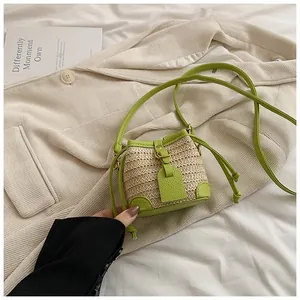 Détail d'un mini sac seau en paille avec bordure vert vif sur fond de blazer blanc cassé
