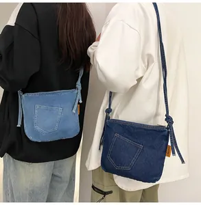 Detail of denim crossbody bucket bag showing orange side logo and knotted shoulder strap