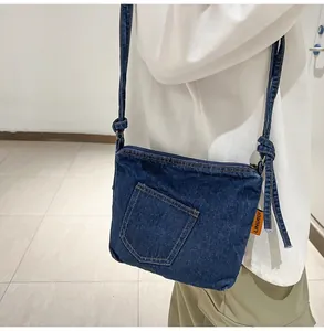 Detail of blue denim bucket crossbody bag with decorative front pocket and orange side label