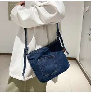 Close-up of blue denim bucket bag featuring knotted shoulder strap and orange logo tag