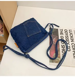 Detail of blue denim crossbody bucket bag featuring a functional pocket and orange woven label