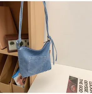 Detail of light blue denim bucket bag featuring stitched pocket and knotted shoulder strap