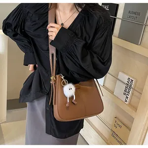 Sac bandoulière en cuir marron avec un porte-clé monstre en peluche sur la lanière