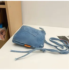 Detail of blue denim crossbody bag featuring orange tag and retro patchwork pocket
