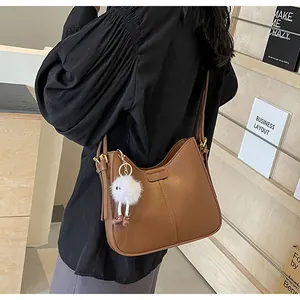 Détail d'un sac hobo en cuir marron avec un joli pendentif de monstre en peluche blanc