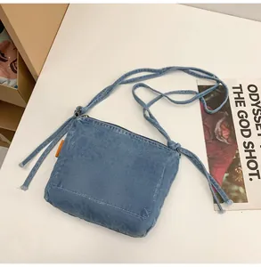Detail shot of blue denim crossbody bag featuring frayed knot straps and orange side tag