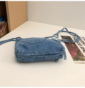 Detail of blue denim crossbody bucket bag featuring vintage pocket design and fabric strap