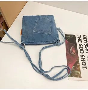 Detailed close-up of a blue denim crossbody bucket bag with orange tag on white background