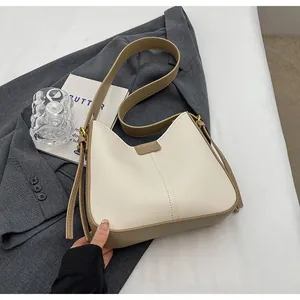 Détail du sac à bandoulière contrasté crème et marron avec boucles dorées sur table blanche