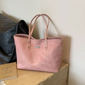 Pink suede tote bag with silver logo plaque shown in a stylish indoor setting