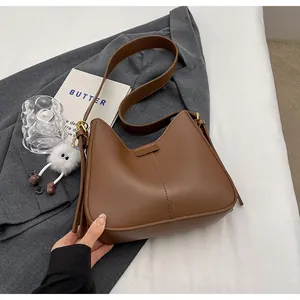 Gros plan du sac hobo en cuir marron avec breloque sur fond de costume gris