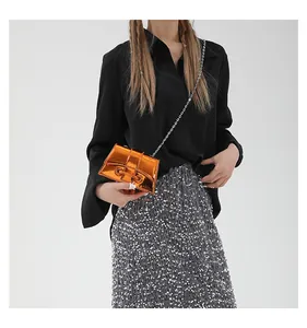 Détail d'un mini sac bandoulière orange brillant en cuir verni avec chaîne argentée