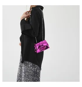 Détail du sac bandoulière en cuir verni fuchsia avec chaîne argentée sur le modèle