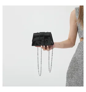 Détail d'un mini sac bandoulière en cuir verni brillant avec chaîne et barre métallique