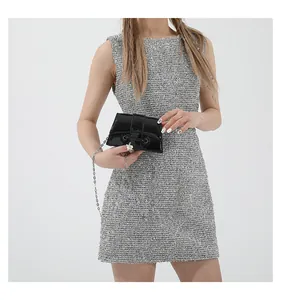 Détail d'un mini sac bandoulière en cuir verni noir avec chaîne argentée sur une robe à paillettes