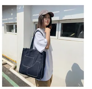 Detail of dark blue denim tote bag featuring white contrast stitching and large pockets