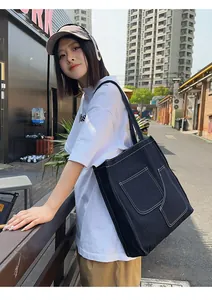 Detail of black denim tote bag featuring white contrast stitching and large front pockets