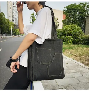 Detail of black denim tote bag with visible yellow stitching and two front patch pockets