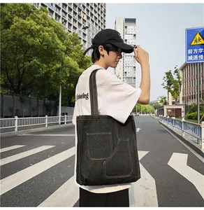 Detail of black denim tote bag with visible contrast stitching and two front patch pockets