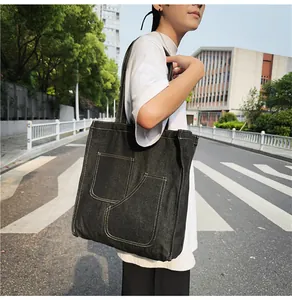 Detail of black denim tote bag with visible white stitching and functional double pockets