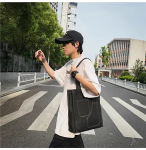 Outdoor street view of a large black denim tote bag with visible contrast stitching detail