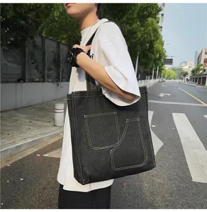 Detail of dark denim tote bag featuring dual front pockets and contrast stitching