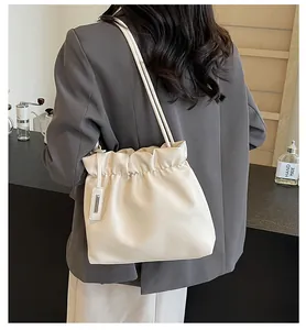 Detail view of cream pleated bucket bag with fine shoulder strap and logo detail