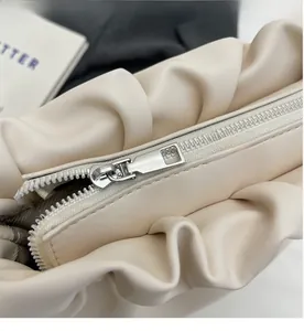 Close-up of smooth silver metal zipper and pleated leather detail on beige bucket bag