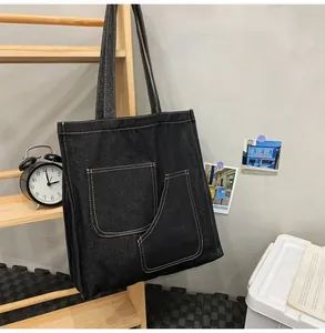 Detail of black washed denim tote bag showing double front pockets and contrast stitching