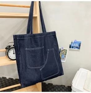 Detail of dark blue denim tote bag with visible white stitching and large front pockets