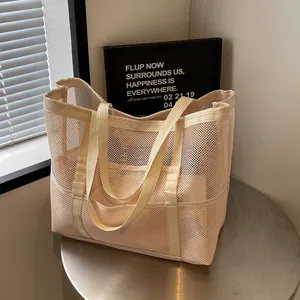 Bolso tote minimalista de malla crema con múltiples bolsillos en un soporte moderno