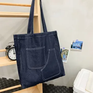 Large dark blue denim tote bag with contrast stitching and double front pockets on wood rack