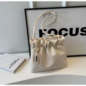 Detailed shot of cream ruched dumpling bag with dual slim straps on geometric stand