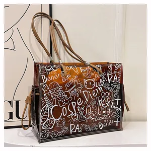Detail view of brown transparent jelly tote bag with white graffiti prints and leather handles
