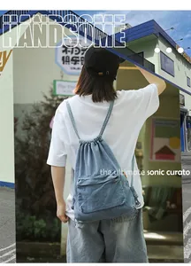 Détail du sac à dos en jean bleu clair avec cordon et poche zippée à l'aspect délavé