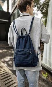 Détail du sac à dos en denim bleu foncé avec fermeture à cordon et poche zippée